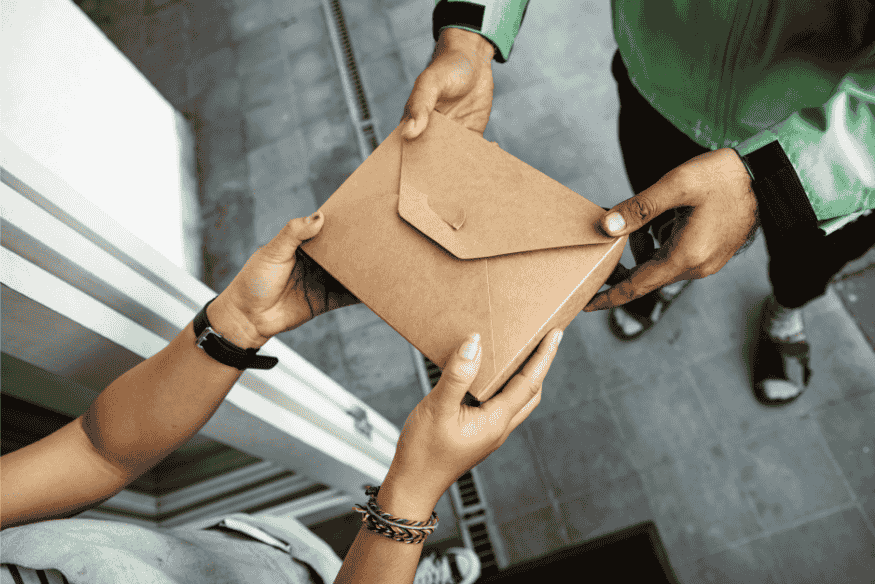Pessoa recebendo um envelope de papel kraft das mãos de um entregador, representando a entrega do RG Pet físico para tutores de cães e gatos.