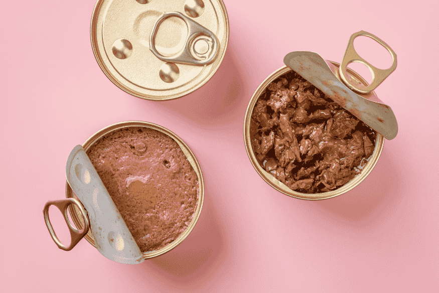 Latas abertas de ração úmida para gatos sobre fundo rosa, representando opções de alimento para filhotes.