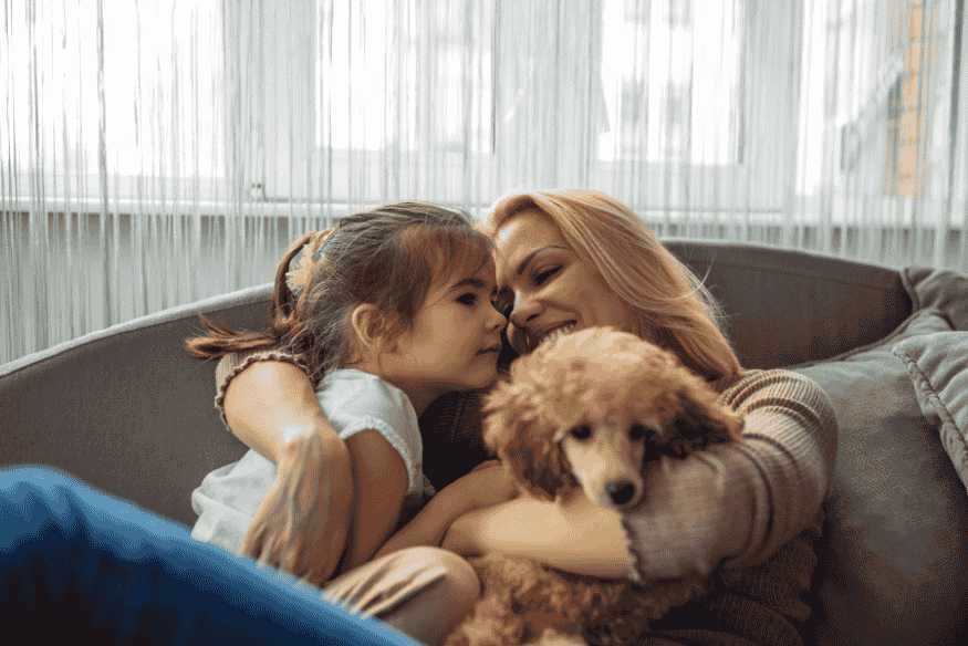 Mãe e filha abraçadas com um cachorro no colo, simbolizando o aprendizado de empatia e cuidado com pets.