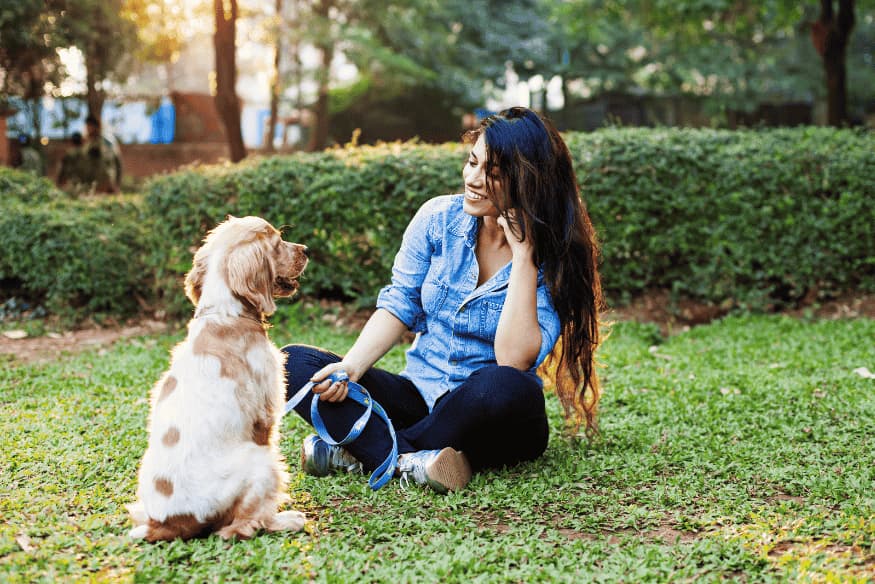 Mulher treinando e socializando seu cachorro em parque, demonstrando vínculo e obediência.