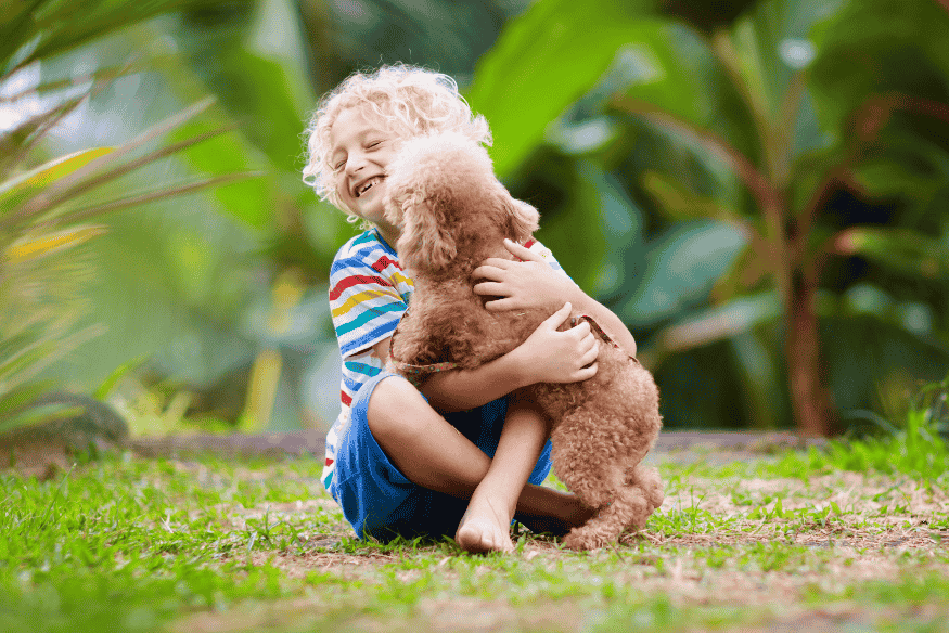 Criança abraçando um filhote de cachorro em ambiente verde, ilustrando o afeto e a criação de laços nos primeiros dias.