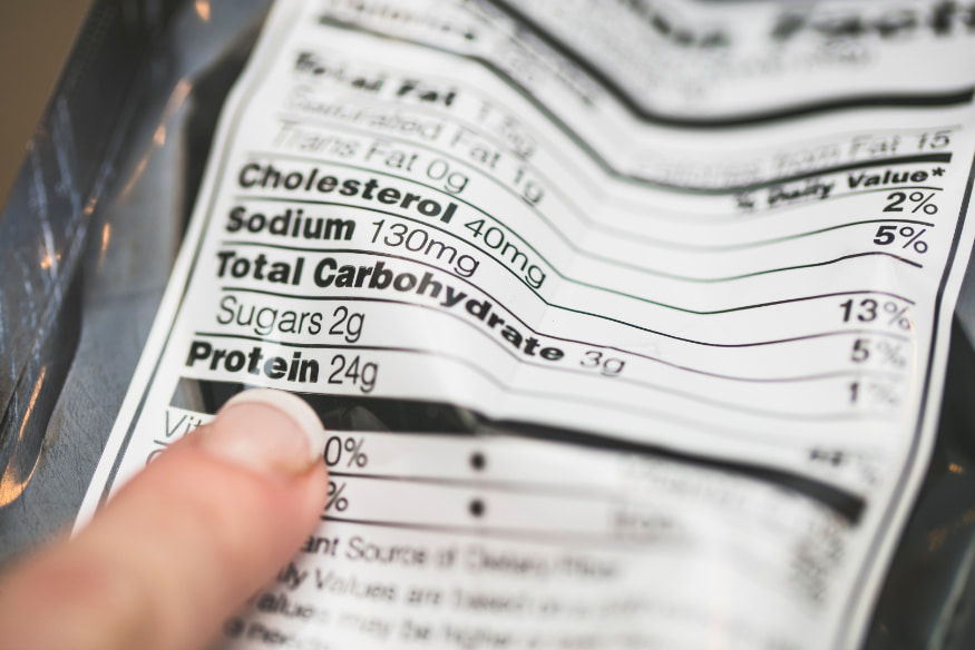 Pessoa apontando para tabela nutricional em rótulo de embalagem, destacando a importância de analisar os ingredientes da ração para pets.