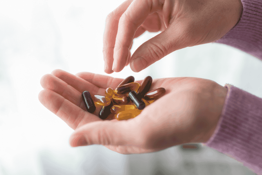 Mãos femininas segurando cápsulas de suplementos vitamínicos variados