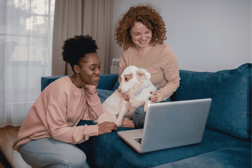 Duas mulheres analisando plano de saúde pet no notebook com o cachorro no colo.