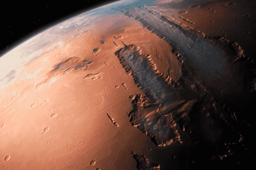 Vista orbital da superfície de Marte mostrando cânions, crateras e extensas formações rochosas em tons avermelhados.