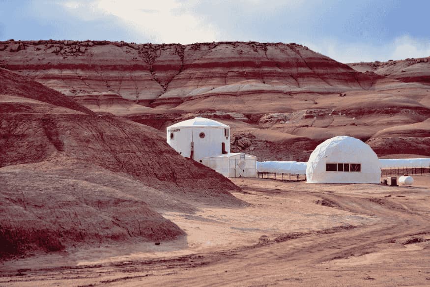 Base de simulação de vida em Marte instalada em terreno árido e avermelhado, com módulos brancos cercados por colinas rochosas.