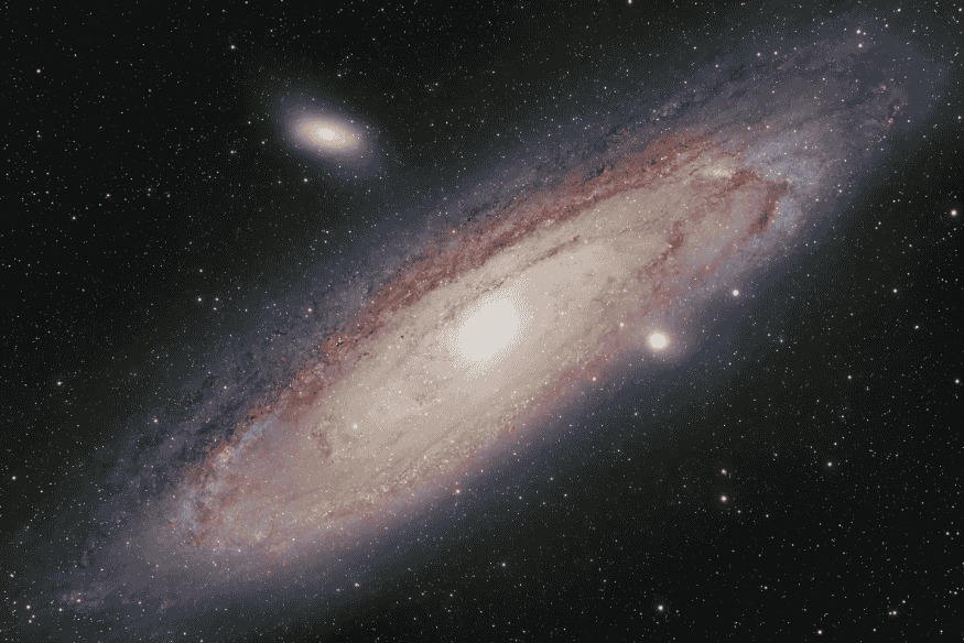 Galáxia de Andrômeda em destaque no espaço, com núcleo muito luminoso, disco extenso e galáxias menores visíveis ao redor.