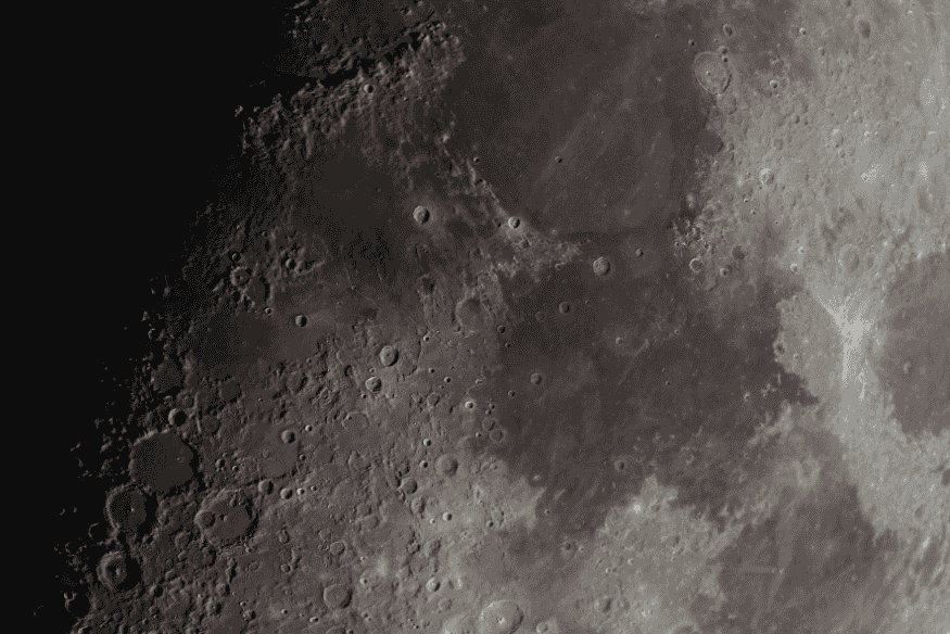 Superfície da Lua vista de perto, com grande quantidade de crateras e relevo acidentado visível na região iluminada do satélite.