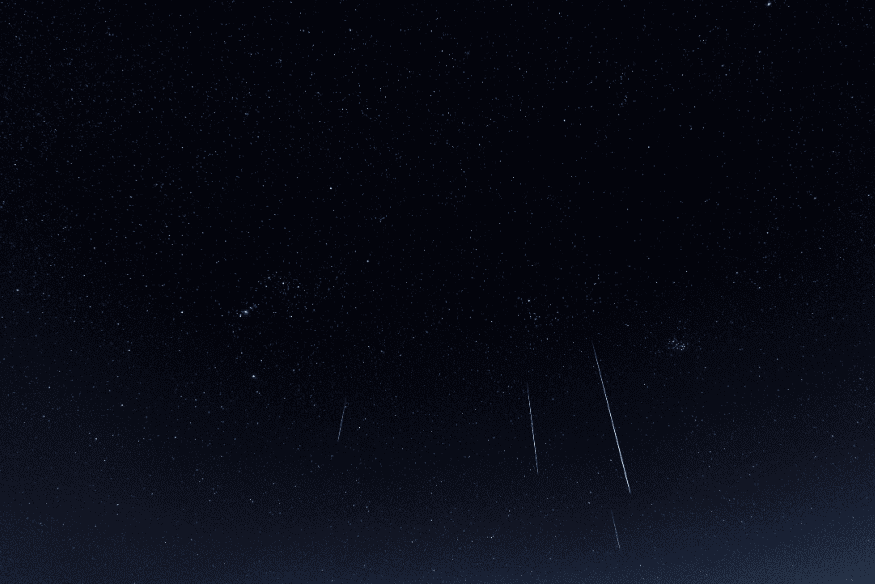 Céu noturno estrelado com rastros luminosos e pontos brilhantes, ilustrando como observar diferenças entre estrelas cintilantes e planetas no céu.