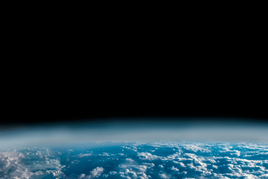 Curvatura da Terra vista do espaço com atmosfera azulada e fundo totalmente escuro, representando a transição entre ambiente com ar e vácuo espacial.