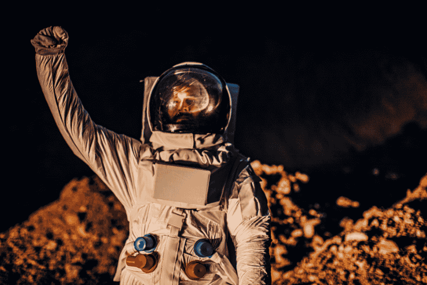 Astronauta em traje espacial com braço erguido sobre terreno rochoso, imagem usada para ilustrar o tema do som no espaço e a explicação da física.