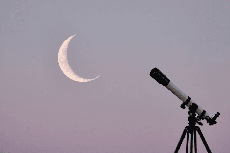 Telescópio montado em tripé ao lado de uma Lua crescente, mostrando situação comum de ajuste de foco para observar a Lua com mais nitidez.