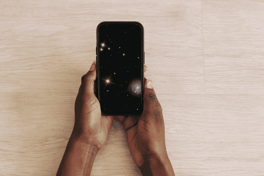 Pessoa segurando um celular com aplicativo ou imagem do céu estrelado na tela, em composição relacionada à observação e fotografia de estrelas com o smartphone.