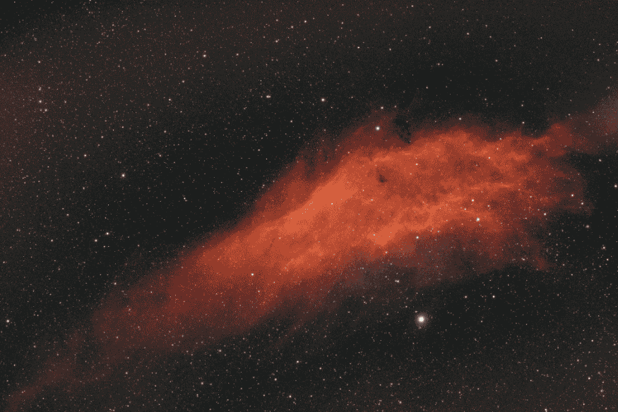 Nebulosa avermelhada alongada em meio a céu repleto de estrelas, mostrando gás iluminado em longa faixa no espaço.