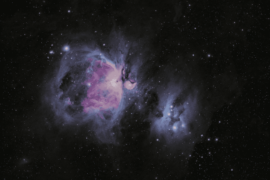 Nebulosa extensa em tons roxos e azulados no espaço profundo, com nuvens de gás iluminadas e estrelas espalhadas ao redor.