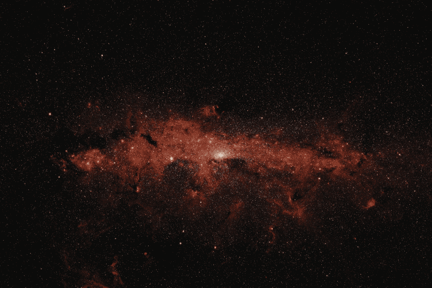 Grande região nebulosa em tons avermelhados com muitas estrelas ao redor, registrada em campo amplo no espaço profundo.