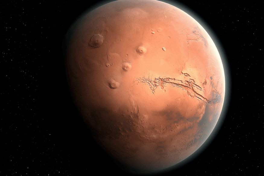 Marte visto no espaço com superfície avermelhada, montes vulcânicos, crateras e o Valles Marineris visível como grande fratura na crosta do planeta.