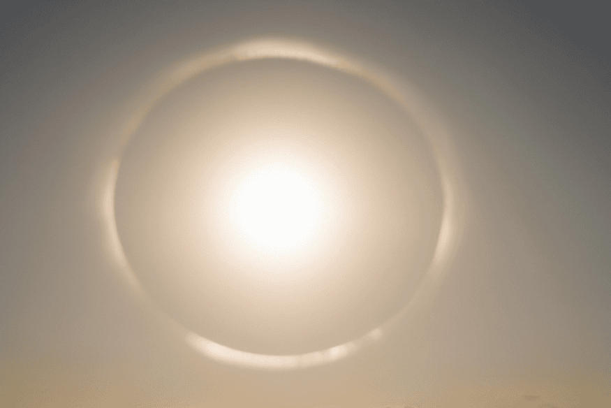 Halo solar circular ao redor do Sol em céu claro, mostrando o anel luminoso típico causado pela refração da luz em cristais de gelo.