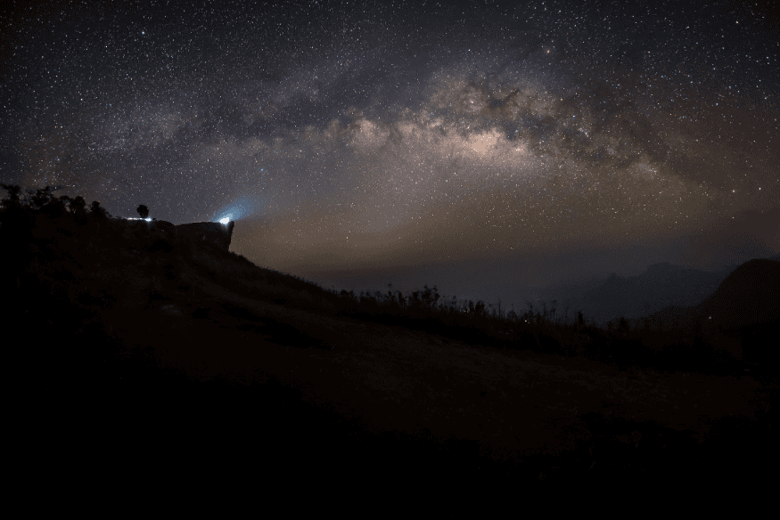 Céu noturno com a Via Láctea sobre montanhas e brilho difuso próximo ao horizonte, possivelmente relacionado à luz zodiacal.