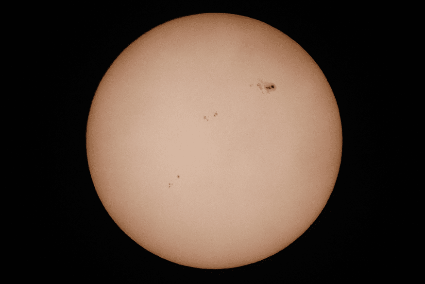 Close da superfície do Sol com várias manchas solares distribuídas pelo disco, incluindo grupo maior na parte superior direita.