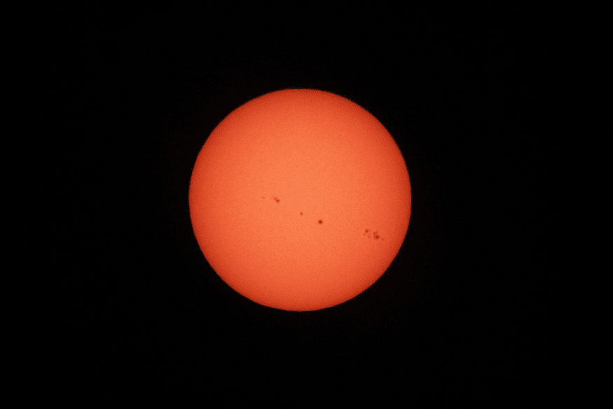 Sol em tom avermelhado com várias manchas solares alinhadas na superfície, imagem usada para ilustrar atividade magnética solar.