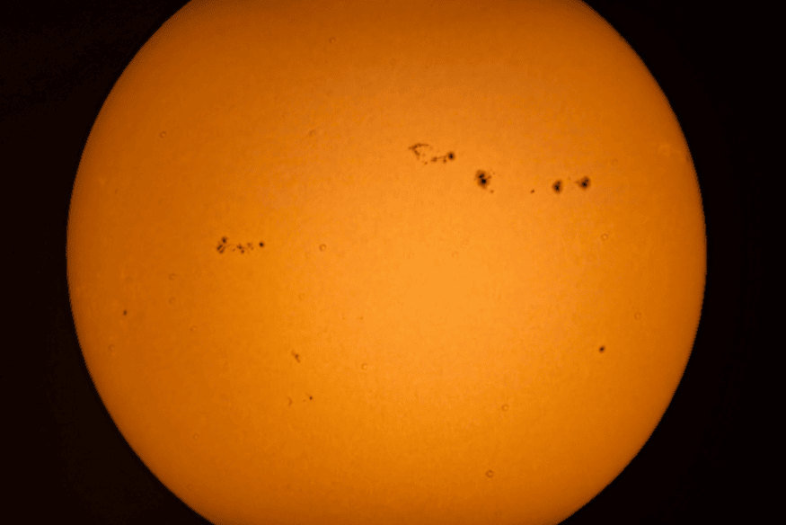 Imagem ampliada do Sol em laranja com diversos grupos de manchas solares bem definidos, mostrando a dinâmica da superfície solar.