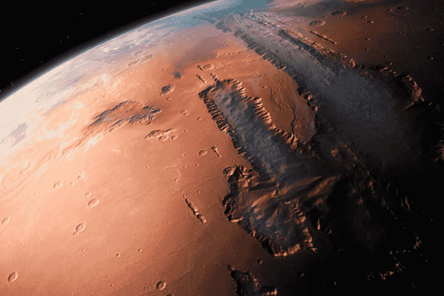 Superfície de Marte vista em perspectiva orbital, com cânions, crateras e relevo acentuado no planeta vermelho.