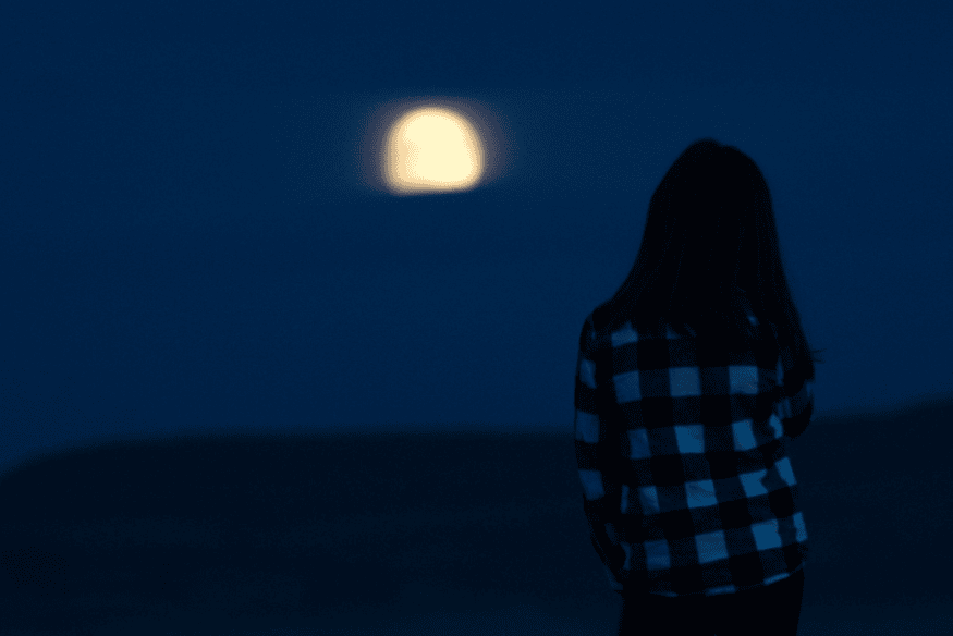 Pessoa olhando para a Lua brilhante no céu azul escuro durante o início da noite, sem uso de equipamentos.