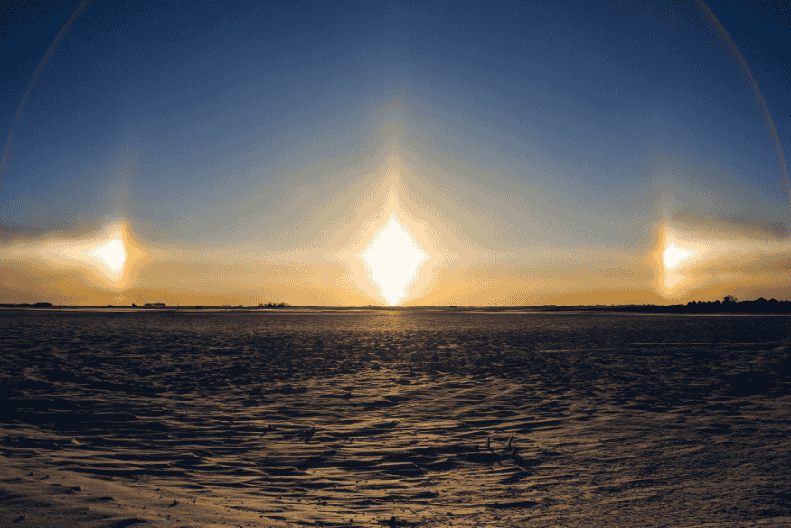 Parélios intensos em ambos os lados do Sol sobre superfície congelada ao entardecer, com halo solar amplo no céu.