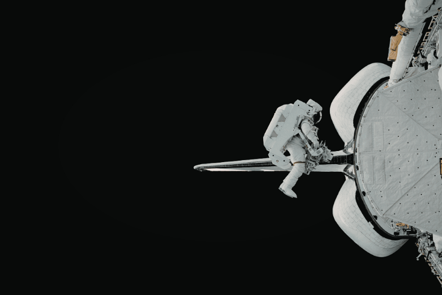 Astronauta realizando atividade extraveicular na parte externa de uma nave espacial, representando trabalho técnico e manutenção no espaço.