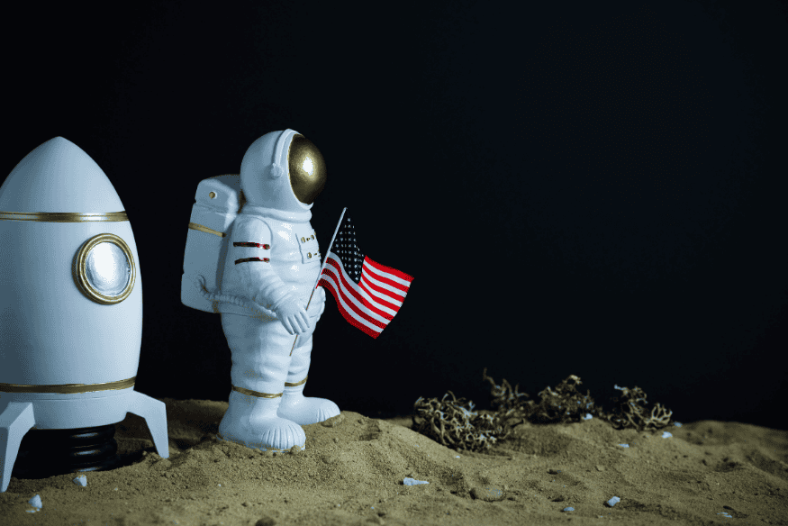 Astronauta ao lado de foguete segurando uma bandeira em cenário espacial, imagem ilustrativa sobre atividades e rotina dos astronautas no espaço.