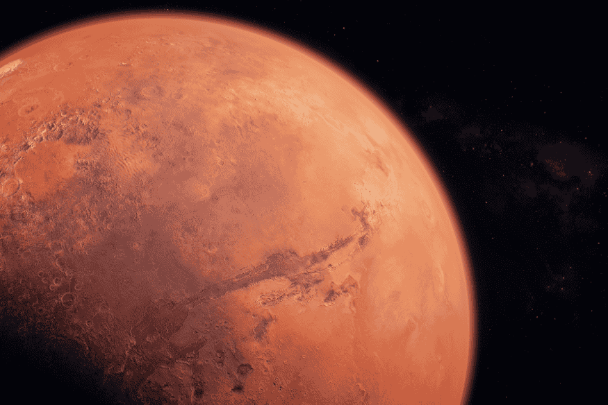 Marte visto do espaço com coloração avermelhada, crateras, planícies e grandes formações geológicas visíveis em sua superfície.