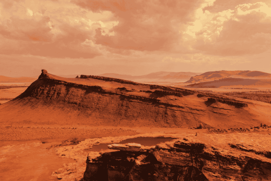Paisagem marciana com terreno seco, formações rochosas, colinas e céu em tons avermelhados, lembrando o ambiente árido do planeta Marte.